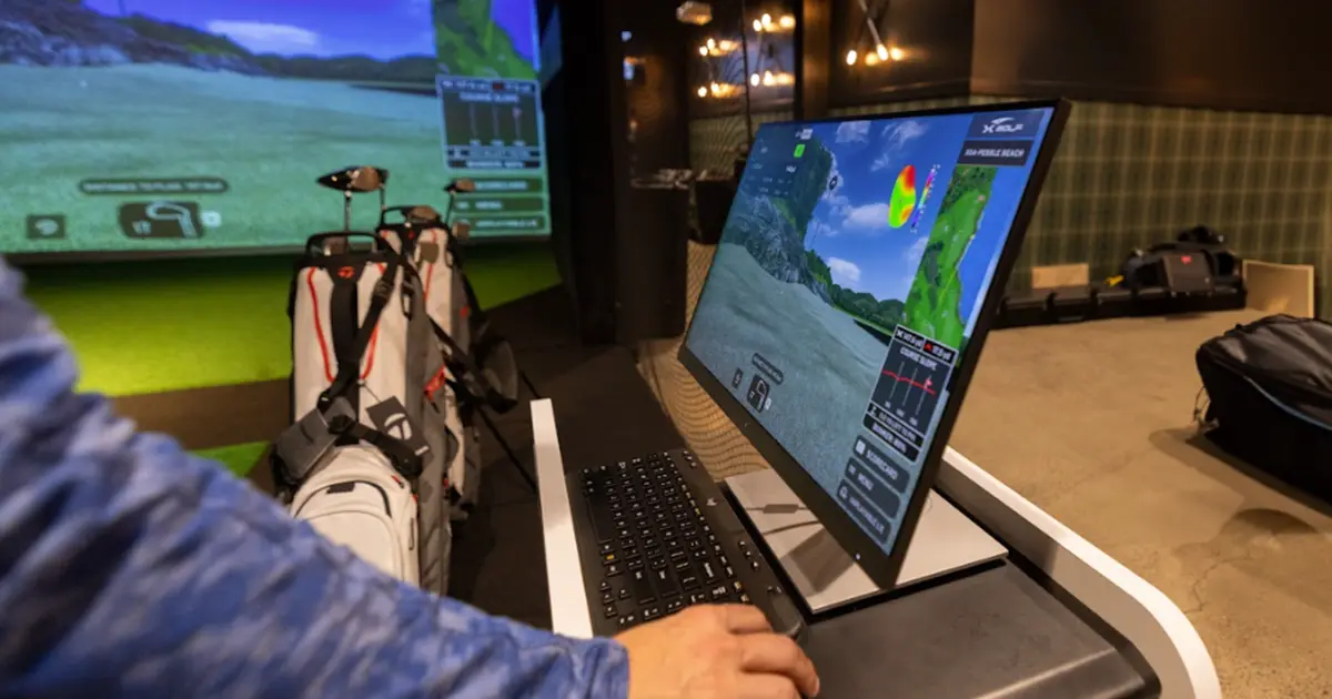 Person interacting with a golf simulator display at X-Golf Frisco, showcasing different golf game modes and performance stats on screen.