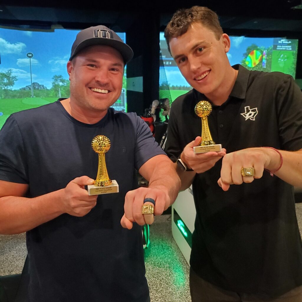 Two men with their X-Golf Frisco league night trophies and rings on their hands displaying they are the winner at X-Golf Frisco indoor league night.