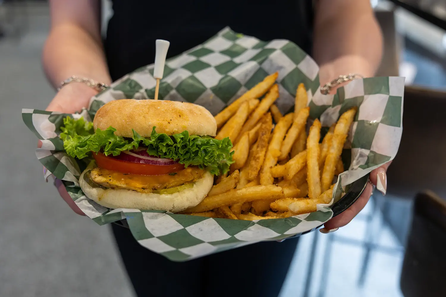 Grilled chicken sandwich with lettuce, tomato, and fries served in a checkered paper basket.