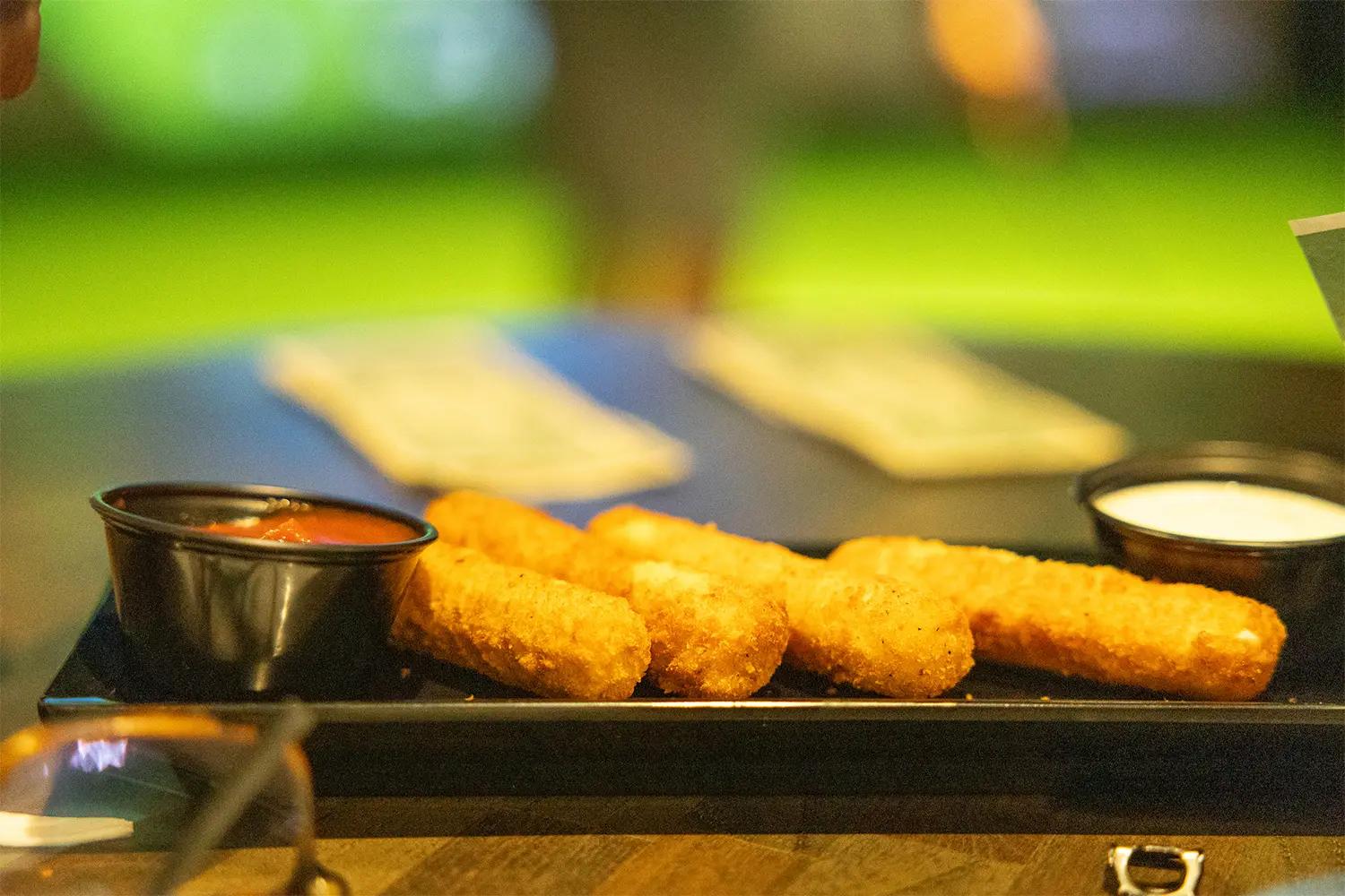 Fried mozzarella sticks served with marinara and ranch dipping sauces on a rectangular black plate.