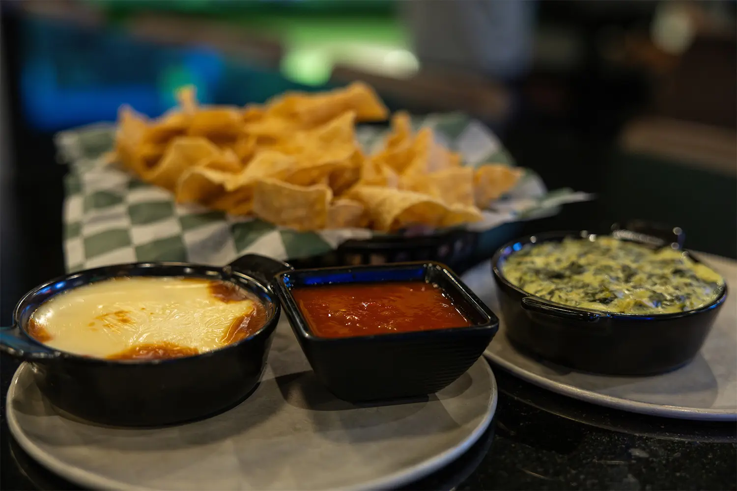 Tortilla chips with three dips: queso, salsa, and spinach artichoke dip.